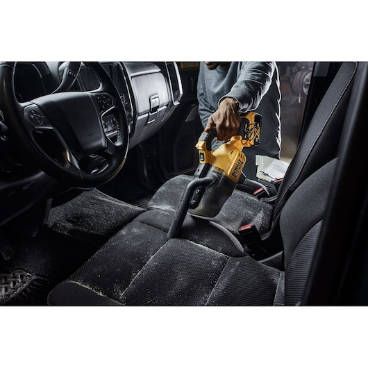 Person using a DEWALT handheld vacuum to clean a dirty car seat interior.