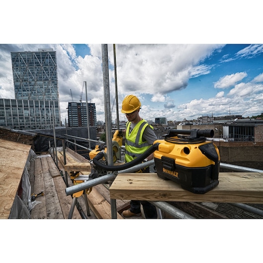 DEWALT DCV584L vacuum used by a worker on a construction site with city buildings and cranes in the background.