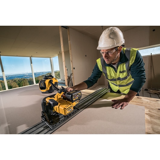 Worker uses a DEWALT cordless saw on a construction site, wearing a helmet and safety vest.