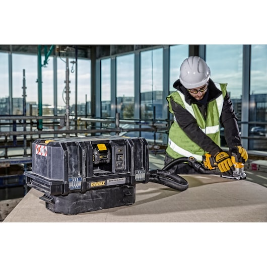 DEWALT DCV586MT2 vacuum on a workbench, with a worker using a tool nearby in a construction setting.