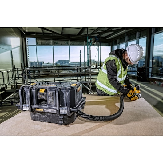 DEWALT vacuum DCV586MT2 used on a jobsite, attached to a tool by a worker wearing safety gear.