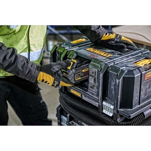 Person installs a DEWALT battery into a rugged DEWALT portable dust extractor on a worksite.