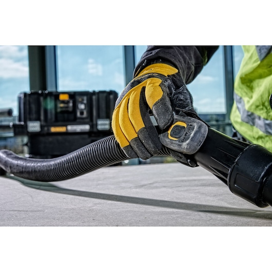 Worker in gloves connects a DEWALT hose to a tool on a construction site, with equipment case in the background.