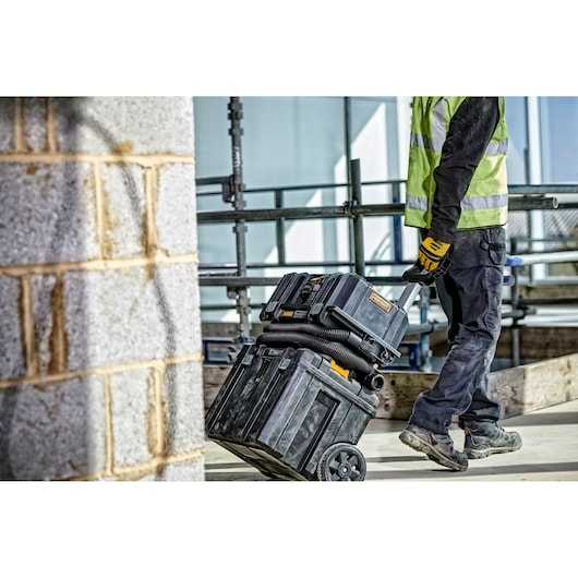 Worker pulls DEWALT DCV586MT2 wheeled tool storage on a construction site.