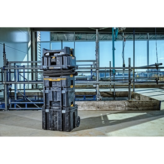 Stacked DEWALT tool storage system with wheels on a construction site, scaffolding and windows in the background.