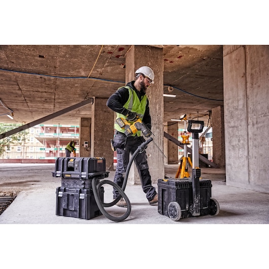 Worker uses DEWALT tools and vacuum on construction site. Equipment stored in rugged black cases.