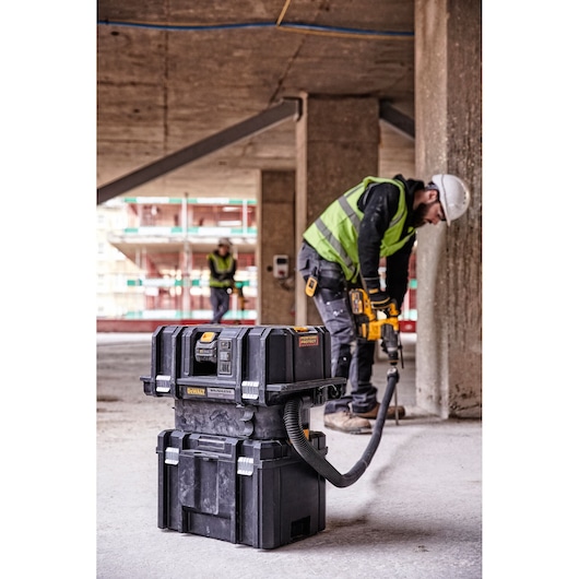 DEWALT DCV586MT2 vacuum on construction site with worker using power tool and dust extraction.