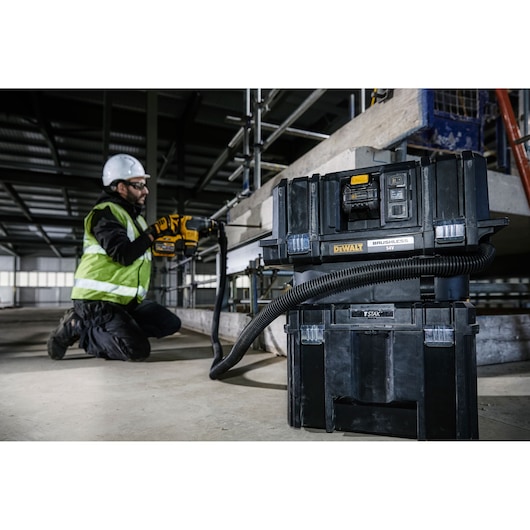 DEWALT DCV586MT2 vacuum in use on a construction site, connected to a tool operated by a worker with safety gear.