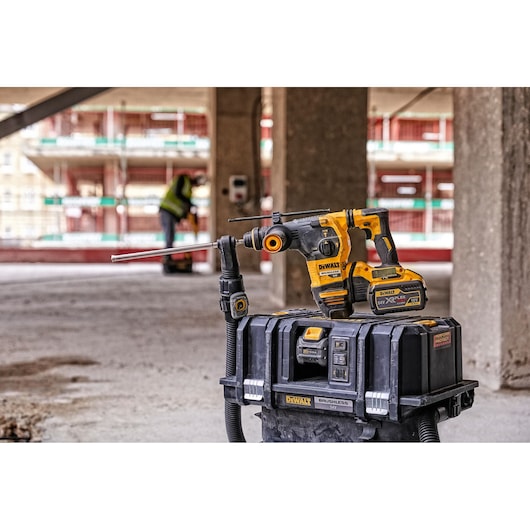 DEWALT cordless drill and toolbox on a construction site with blurred worker in background.