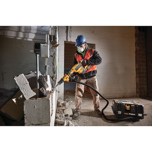 Worker uses DEWALT DCV586MT2 vacuum and demolition tool to break concrete blocks at a construction site.