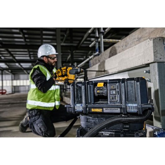 DEWALT DCV586MT2 vacuum at a construction site. Worker in safety gear uses a DEWALT tool near concrete.