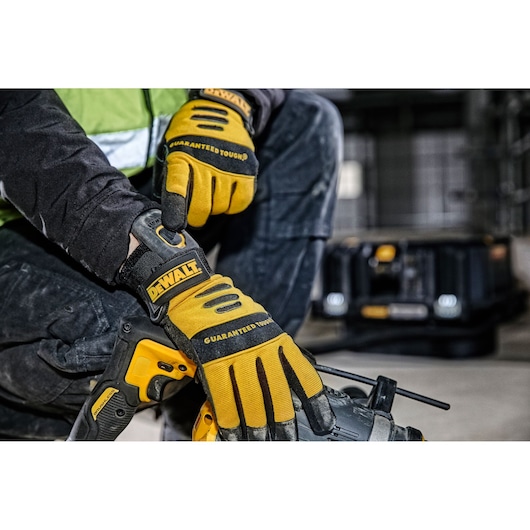 Person wearing DEWALT gloves working with a power tool in a workshop. DEWALT toolbox is visible in the background.