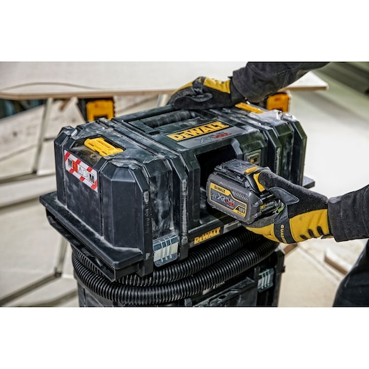 DEWALT DCV586M dust extractor with a person installing a battery on a jobsite.