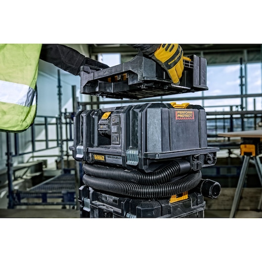 Worker places tray on DEWALT DCV586M cordless dust extractor at a construction site.