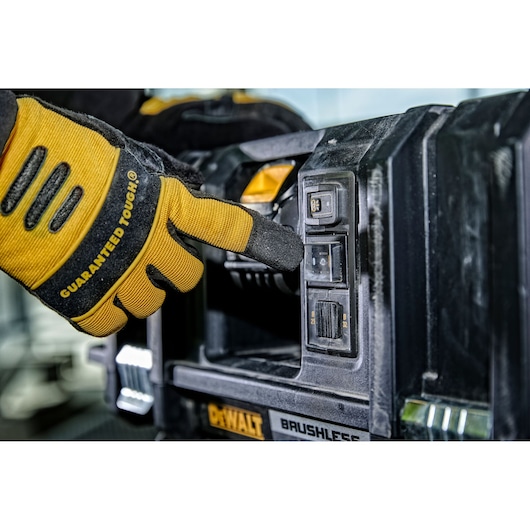 Gloved hand pressing a button on a DEWALT brushless power tool, close-up view of tool controls and branding.