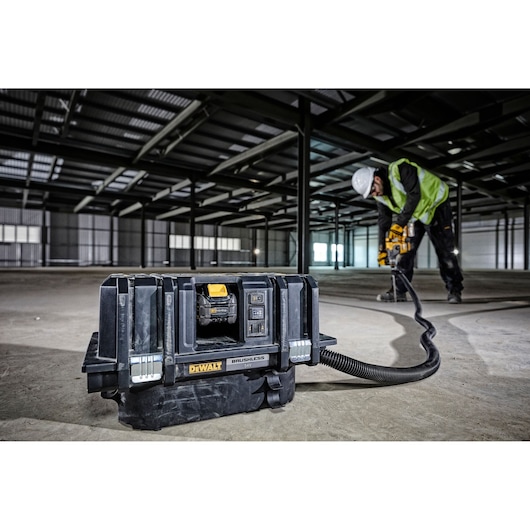 DEWALT DCV586M industrial vacuum in warehouse, worker using power tool connected by hose.