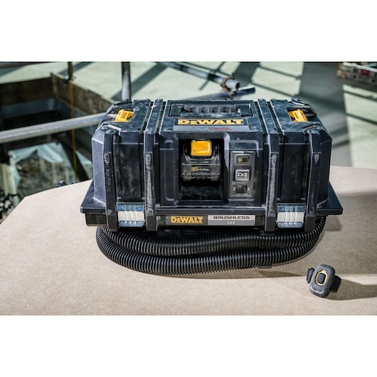 A DEWALT DCV586M 54V brushless portable dust extractor with hose and remote control sits on a workbench.