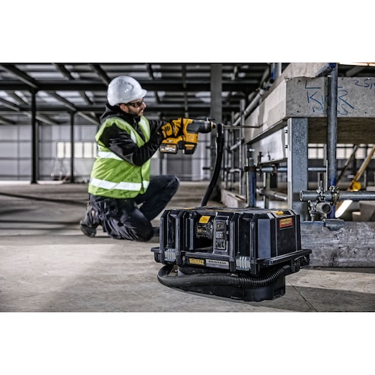DEWALT DCV586M vacuum in use at a construction site with a worker drilling nearby.