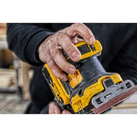 Close-up of a hand adjusting a DEWALT DCW200P2 cordless sander in a workshop setting.