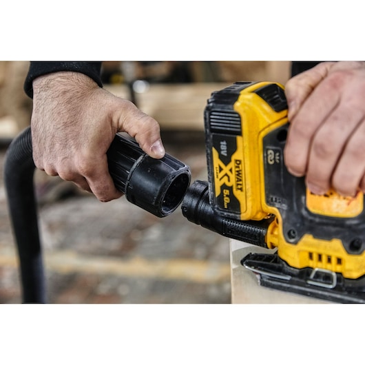 Hands connecting a hose to a DEWALT XR 18V power tool on a workbench.