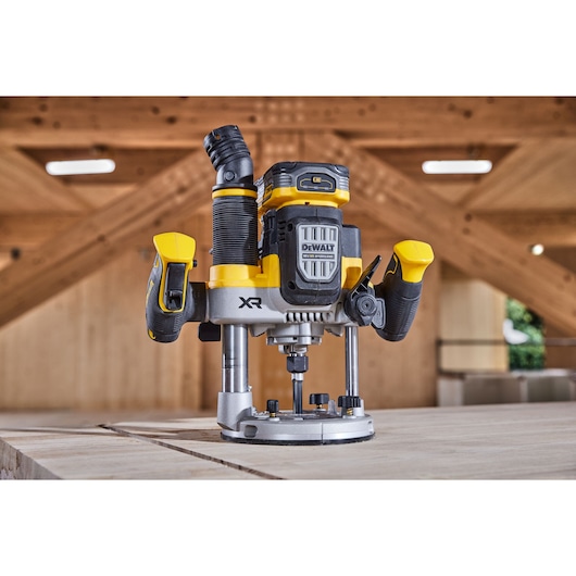 DEWALT XR router tool with handle and dust extraction attachment shown on wooden workbench in workshop setting.