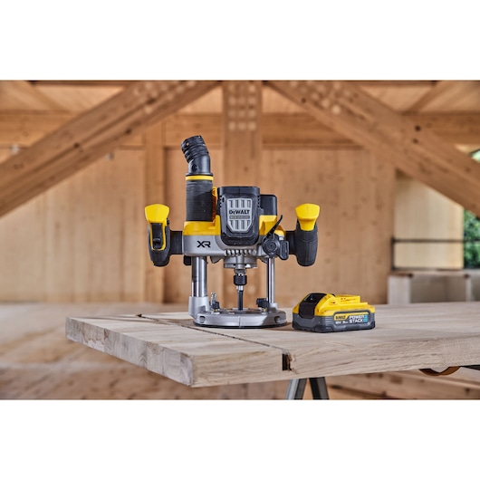 DEWALT router and battery on wooden workbench in carpentry workshop with exposed beams.