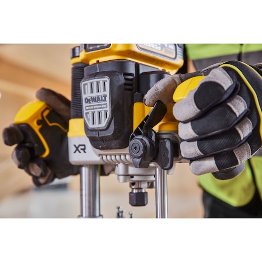 Person wearing gloves adjusts a DEWALT XR router tool in a workshop.