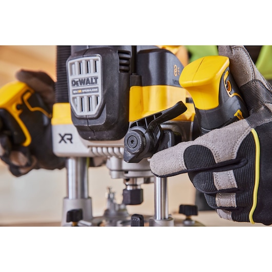 Close-up of a DEWALT XR brushless router being adjusted by a gloved hand during woodworking.