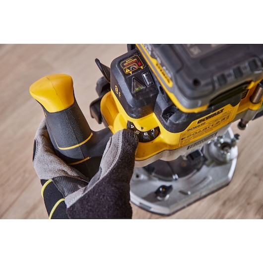 Gloved hand adjusts speed on a DEWALT DCW620H2 power tool placed on a wooden surface.