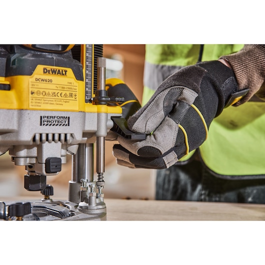 Gloved hand adjusting a DEWALT DCW620 router on a wooden surface, close-up view of the tool and control.