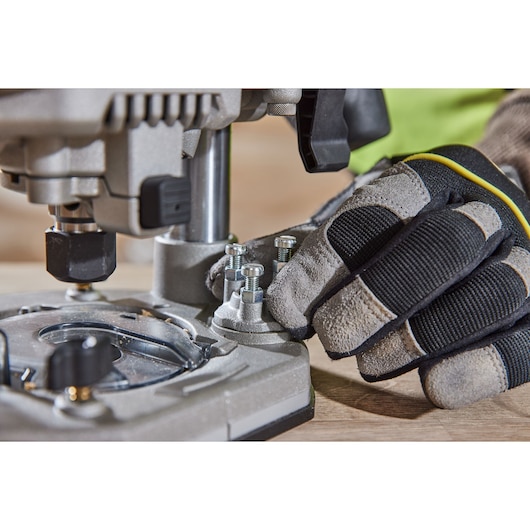 Gloved hand adjusts bolts on a DEWALT power tool set on a wooden surface, close-up industrial scene.