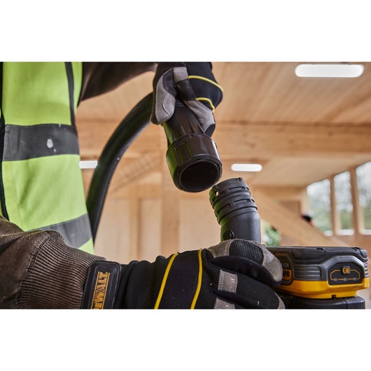 Gloved hands connecting two DEWALT tool hoses in a wooden workshop, focusing on black hose ends.