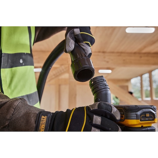 Gloved hands connecting DEWALT power tool hose in wood workspace.