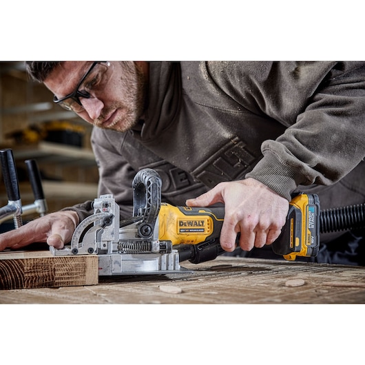 Person using a DEWALT DCW682N cordless joiner tool to work on wood in a workshop setting.