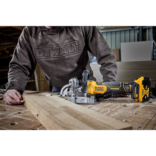 Person uses DEWALT DCW682N cordless joiner tool on wooden board in workshop.