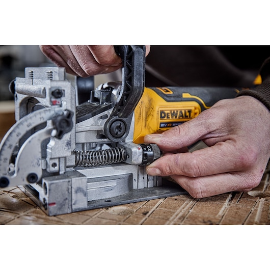 Close-up of hands adjusting a DEWALT woodworking tool on a wooden surface.