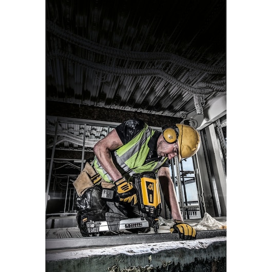 Worker using a DEWALT tool wearing safety gear at a construction site, focused on measuring and drilling metal.