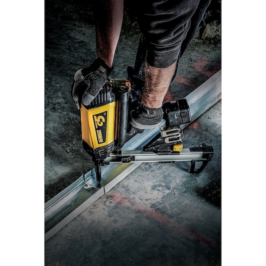 Person using a DEWALT nail gun to secure metal framing to the floor while wearing gloves and work boots.