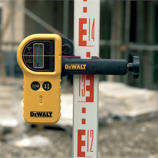 DEWALT laser level with DE0772, DE0772-XJ, attached to a measuring staff on a construction site.