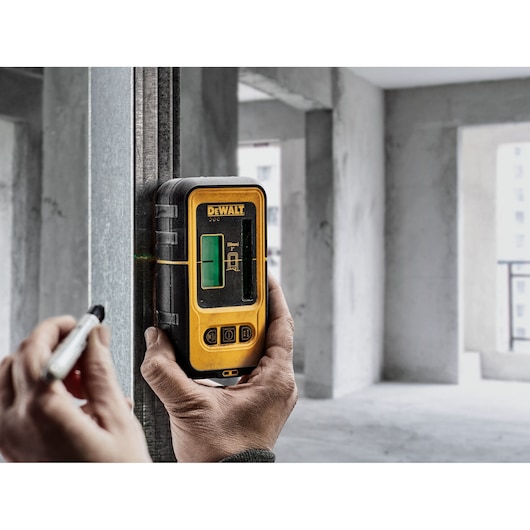 Person uses DEWALT laser detector DE0892G on a metal beam in an unfinished building interior.