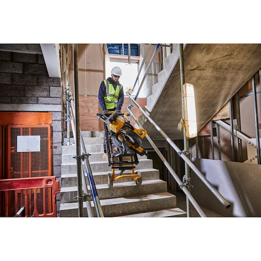 Worker moves DEWALT saw and stand up stairs at a construction site with safety rails and barriers visible.