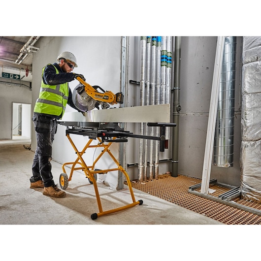 Worker using DEWALT DE7260 saw stand with miter saw indoors at a construction site.
