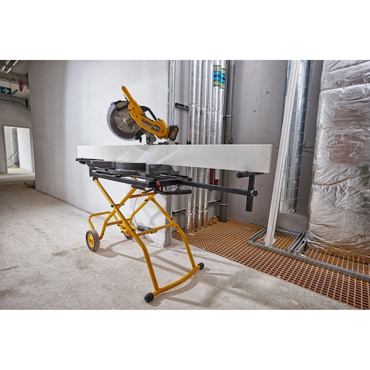 DEWALT DE7260 saw stand with mounted saw in an industrial indoor workspace with pipes and insulation visible.