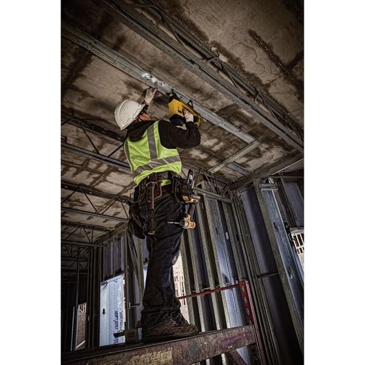 Worker using DEWALT DGN845D1-QW, DGN845D1 tool on ceiling at construction site. Photography category.