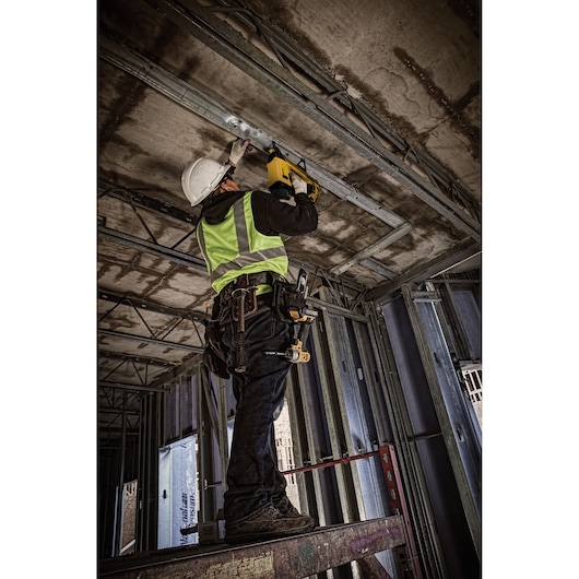 Worker using DEWALT DGN845D1-QW, DGN845D1 tool on ceiling at construction site. Photography category.