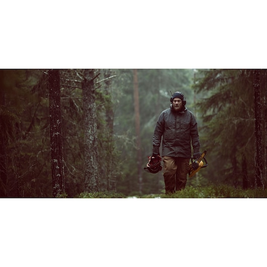 Person in safety gear holding a DEWALT chainsaw and helmet, walking in a misty forest.