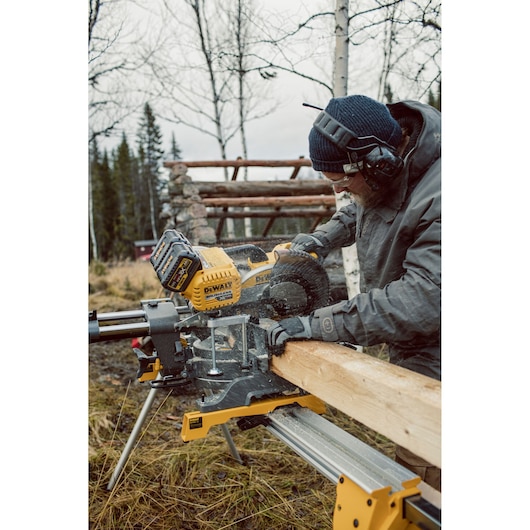 Person using a DEWALT DHS780N saw to cut wood outdoors, wearing gloves and protective headphones.