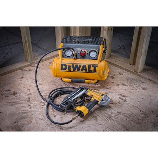 DEWALT air compressor and nail gun with hose on a construction site with wood framing in the background.
