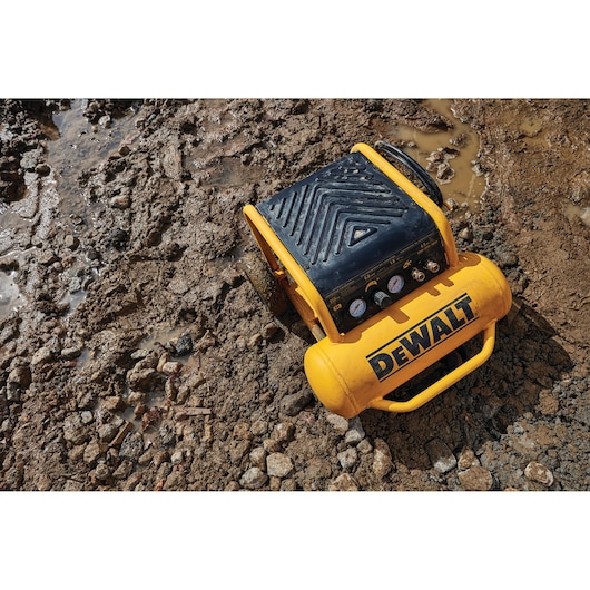 A yellow DEWALT air compressor positioned on a muddy and rocky outdoor ground, showing its rugged design suitable for tough working conditions.