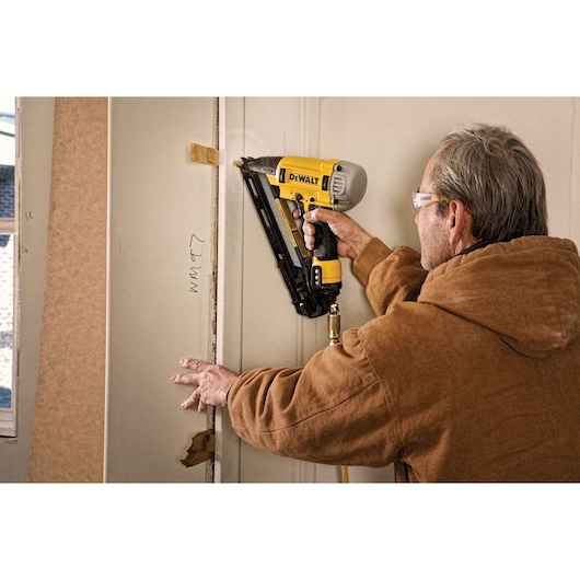 Person using a DEWALT nail gun to attach trim to a door frame during construction or renovation work.